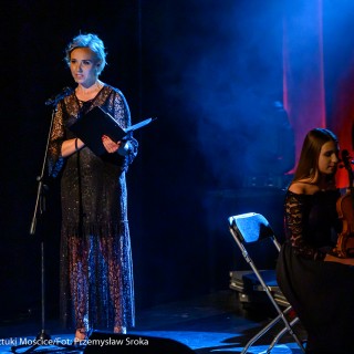 Koncert muzyki filmowej - Crushed Sounds BigBand - Kobieta stoi na scenie, w rękach trzyma podkładkę i mówi do mikrofonu.  - Fot. Przemysław Sroka