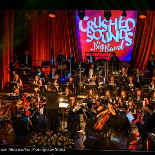 Koncert muzyki filmowej - Crushed Sounds BigBand - Orkiestra gra na scenie, za nimi na ekranie wyświetla się napis "Crushed Sounds + Big Band". - Fot. Przemysław Sroka