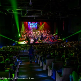 Koncert muzyki filmowej - Crushed Sounds BigBand - Na scenie gra orkiestra, za nimi na ekranie wyświetla się napis "Crushed Sounds + Big Band", na widowni siedzą ludzie i oglądają występ, na salę pada zielone światło z reflektorów.  - Fot. Przemysław Sroka