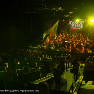Koncert muzyki filmowej - Crushed Sounds BigBand - Na scenie gra orkiestra, za nimi na ekranie wyświetla się napis "Crushed Sounds + Big Band", na widowni siedzą ludzie i oglądają występ, na salę pada zielone światło z reflektorów.  - Fot. Przemysław Sroka