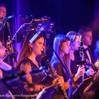 Koncert muzyki filmowej - Crushed Sounds BigBand - Grupa kobiet siedzi na krzesłach i gra na klarnetach patrząc w nuty, pada na nich różowe światło. - Fot. Przemysław Sroka