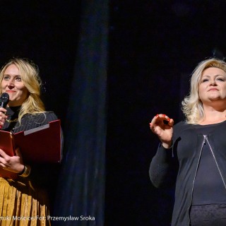 "Four Seasons" - Akrobatyczny Teatr Tańca Mira-Art. Scena Otwarta 2021 - Dwie kobiety stoją na scenie. Blondwłosa kobieta po lewej stronie trzyma mikrofon w prawej ręce, zaś w lewej czerwoną teczkę. Kobieta z prawej gestykuluje rękoma. - Fot. Przemysław Sroka