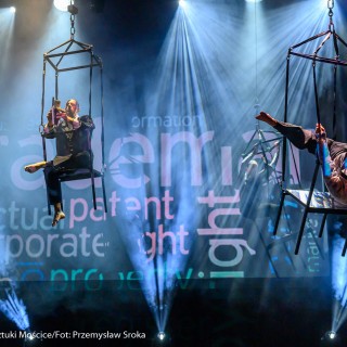"Four Seasons" - Akrobatyczny Teatr Tańca Mira-Art. Scena Otwarta 2021 - Trzech artystów znajduje się na wiszących rekwizytach i wykonuje różne akrobatyczne figury. Tło stanowią duże napisy oświetlone janoniebieskimi światłami. - Fot. Przemysław Sroka