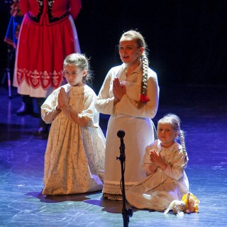 "Kwiat polskiej ziemi" - spektakl o bł. Karolinie w wykonaniu ZPiT Świerczkowiacy - Trzy osoby klęczą na scenie. Pośrodku znajduje się dorosła kobieta, a po lewej i prawej stronie dwie dziewczynki. Obok młodszej z nich leży lalka. Każda z artystek ma złożone ręce w geście modlitwy. Ubrane są one w jasne sukienki, a włosy mają zaplecione w warkocz. - Fot. Jerzy Bardel