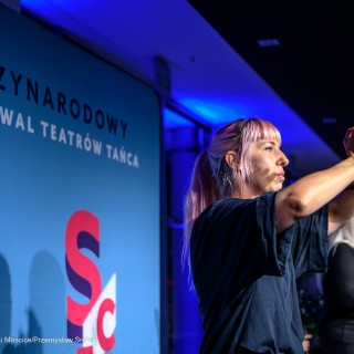 Wernisaż wystawy "Performance Dance" - Karolina Mika stoi na scenie przed mikrofonem i unosi ręce w górę. - Fot: Przemysław Sroka