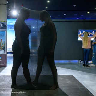 Wernisaż wystawy "Performance Dance" - Dwie kobiety ukryte pod czarnym materiałem tańczą w holu. W tle dwie inne kobiety oglądają wystawę multimedialną. - Fot: Przemysław Sroka