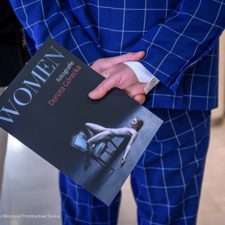 "Women" - wystawa fotografii Doroty Góreckiej - Mężczyzna stoi odwrócony tyłem. Za plecami trzyma folder "WOMEN fotografie Dorota Górecka". - Fot: Przemysław Sroka