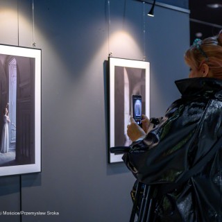 "Women" - wystawa fotografii Doroty Góreckiej - Kobieta stoi w holu, trzyma w dłoniach telefon i robi zdjęcie fotografii. - Fot: Przemysław Sroka