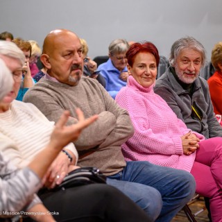 Senior w Centrum - koncert chóru Siemaszki - Publiczność siedzi na krzesłach. Dwie kobiety rozmawiają. Kobieta i mężczyzna patrzą w obiektyw i uśmiechają się. - Fot: Przemysław Sroka
