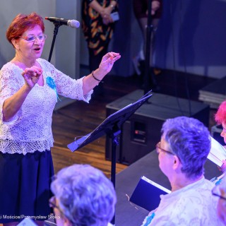 Senior w Centrum - koncert chóru Siemaszki - Dyrygentka stoi przed chórzystkami i dyryguje. - Fot: Przemysław Sroka